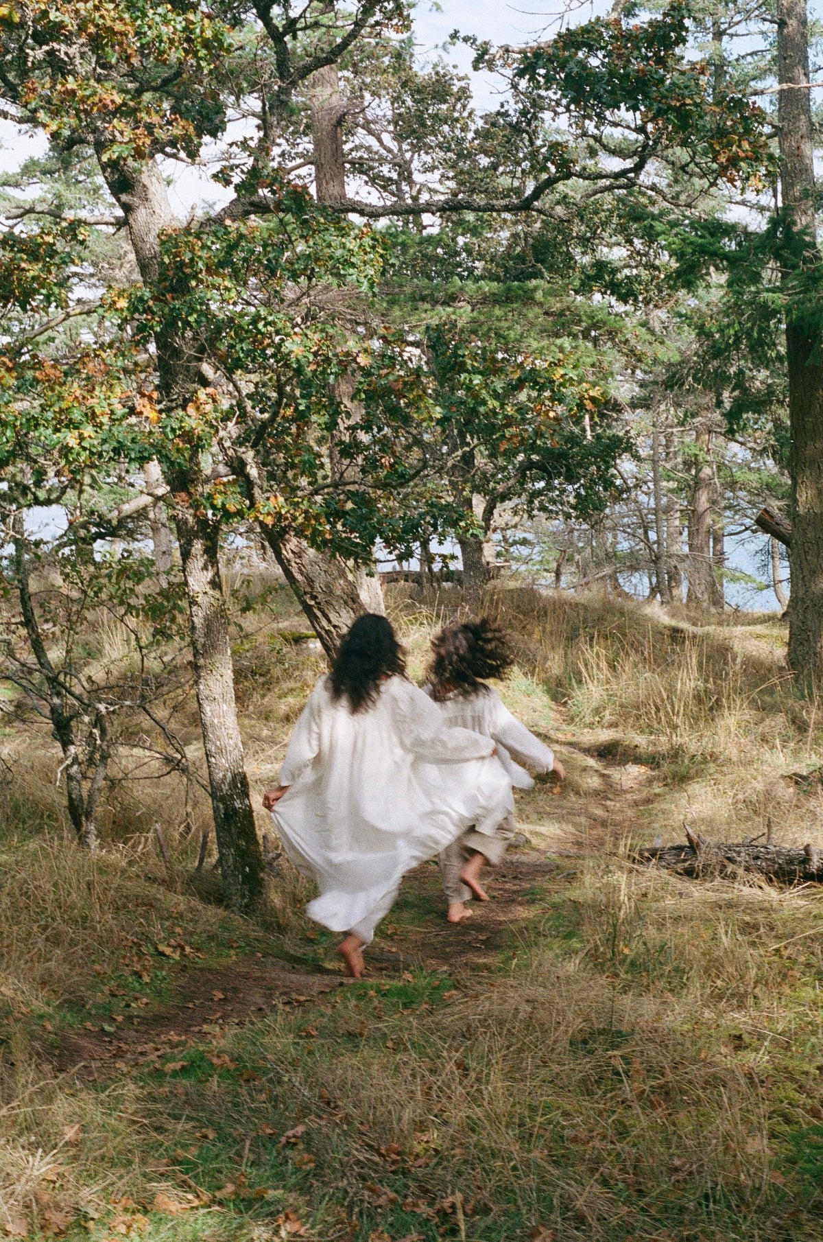 Two women in white dresses walking through a forest path.