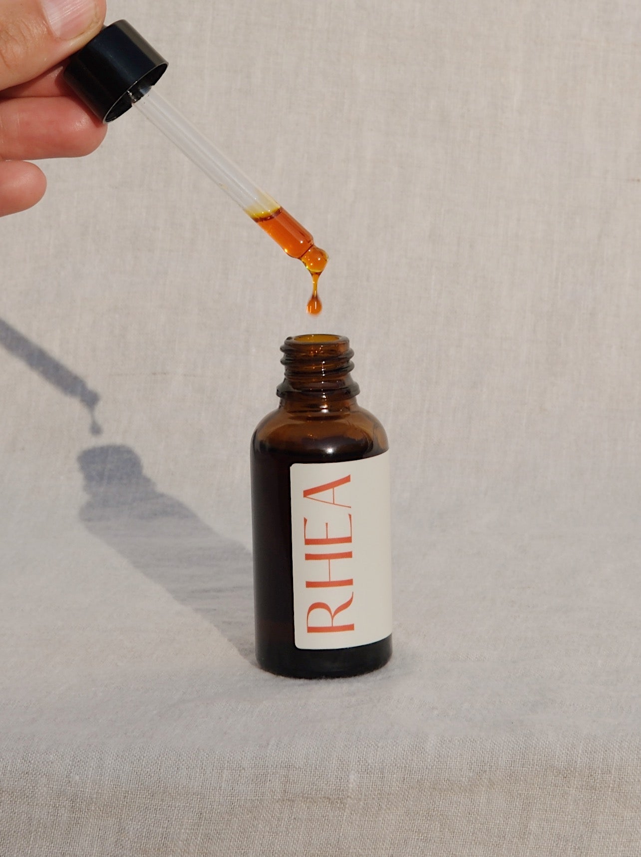 antioxidant face serum by rhea in an amber bottle with a linen background