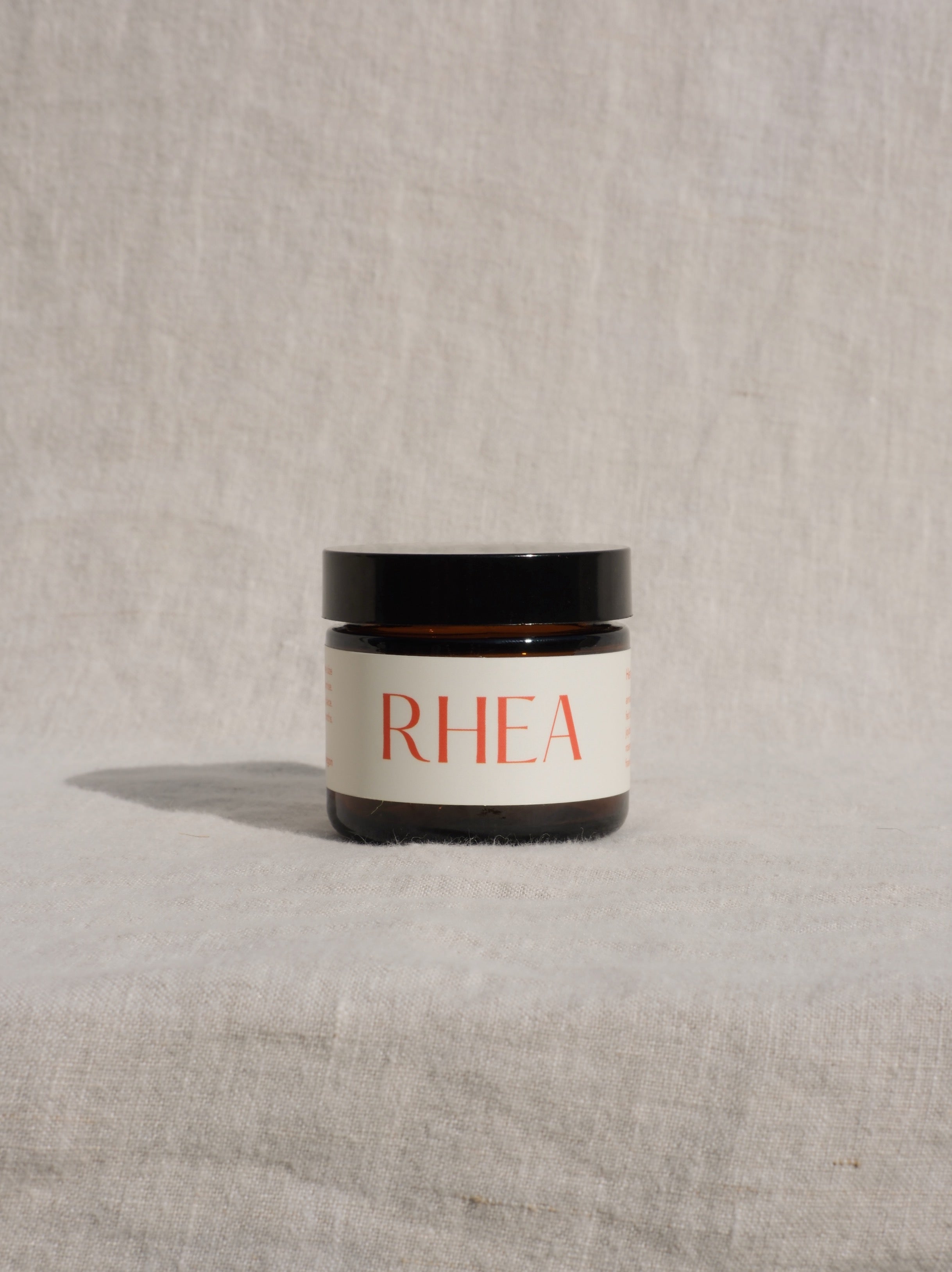 Amber jar of Hera Tallow Face balm with RHEA label on a textured beige background