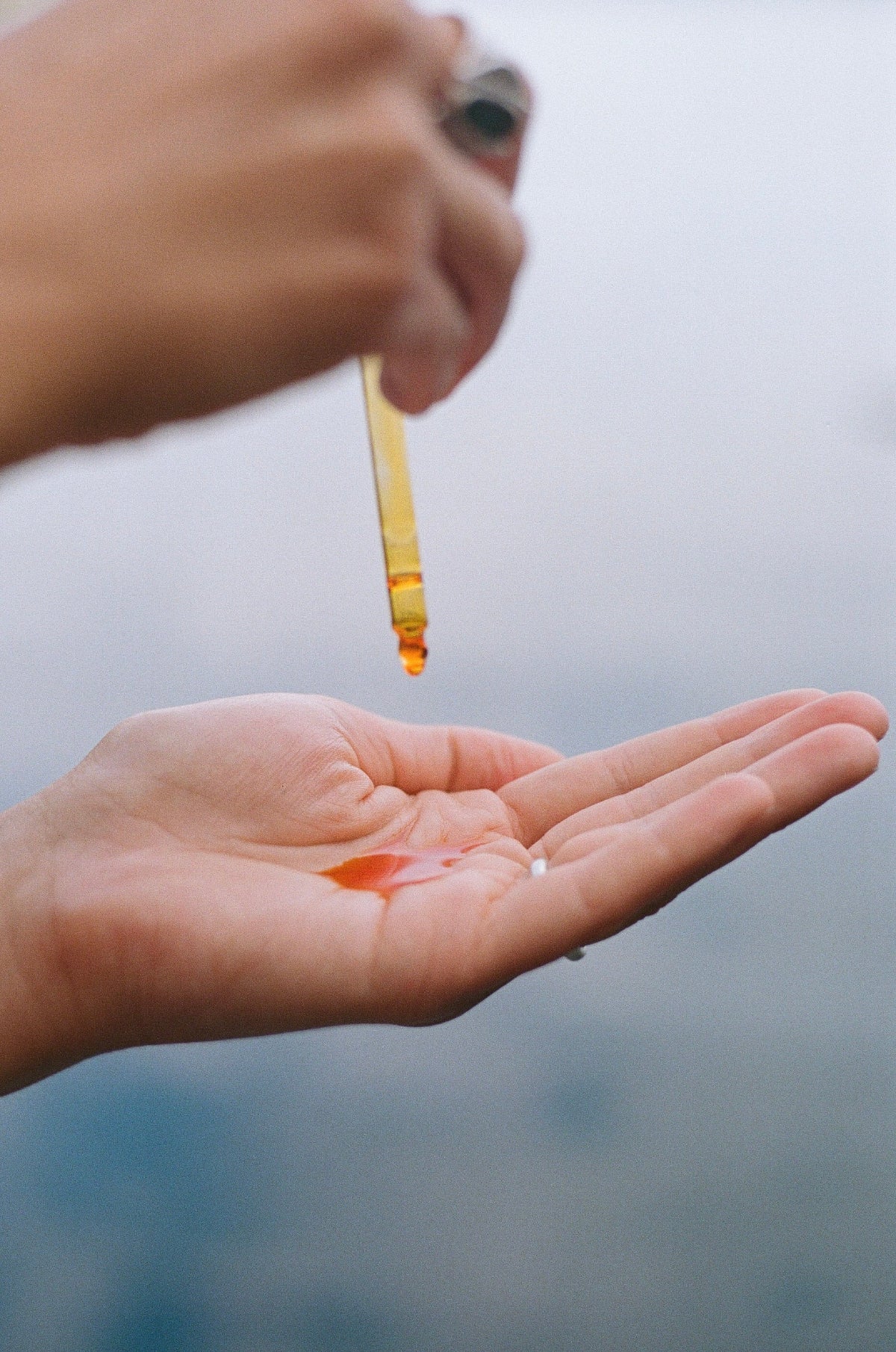 Hand holding a dropper with artemis night serum over another hand