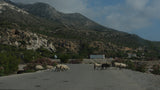 sheep crossing the road with greek mountains in the background