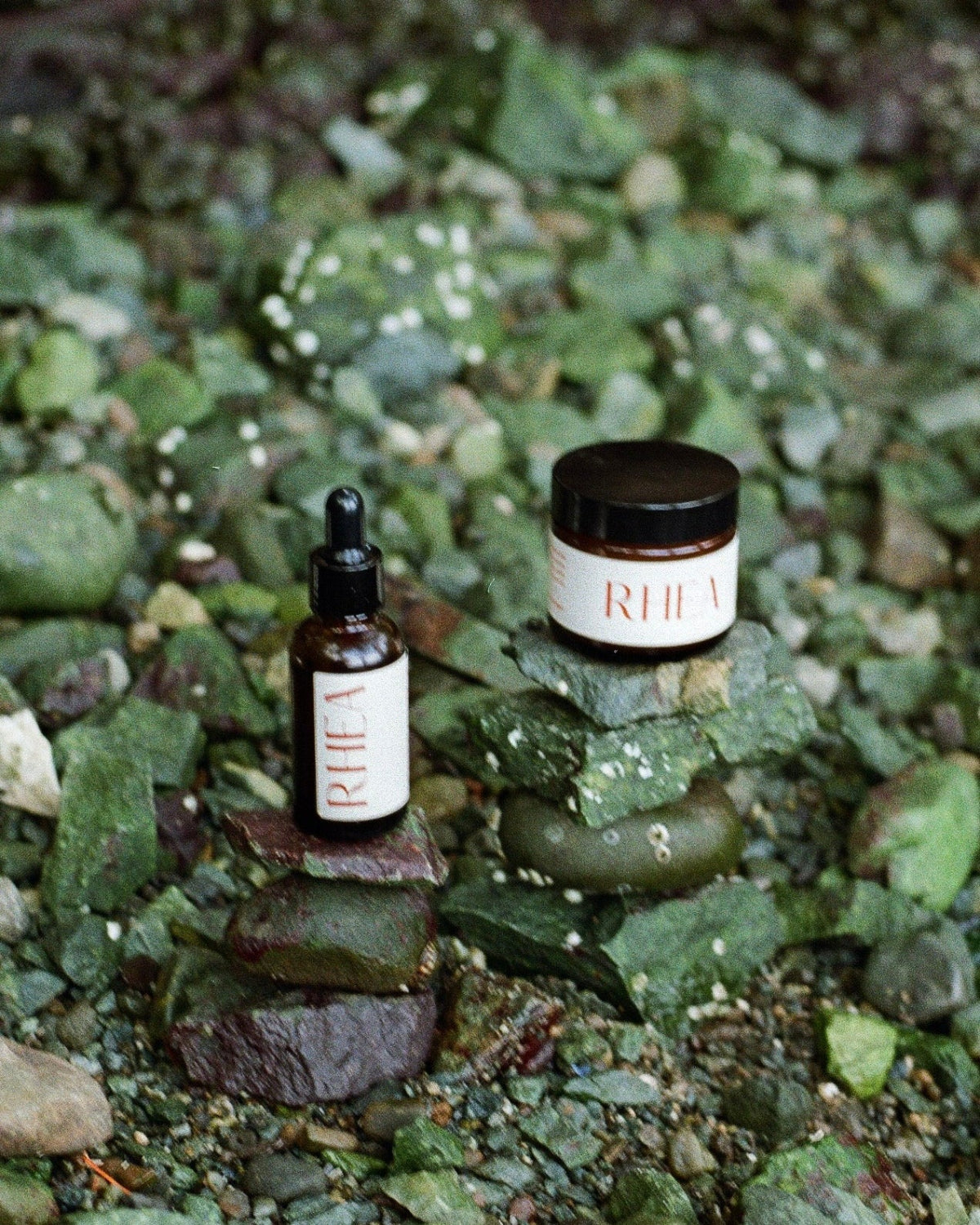 Two rhea skincare products made in oregon and washington on a bed of green rocks 
