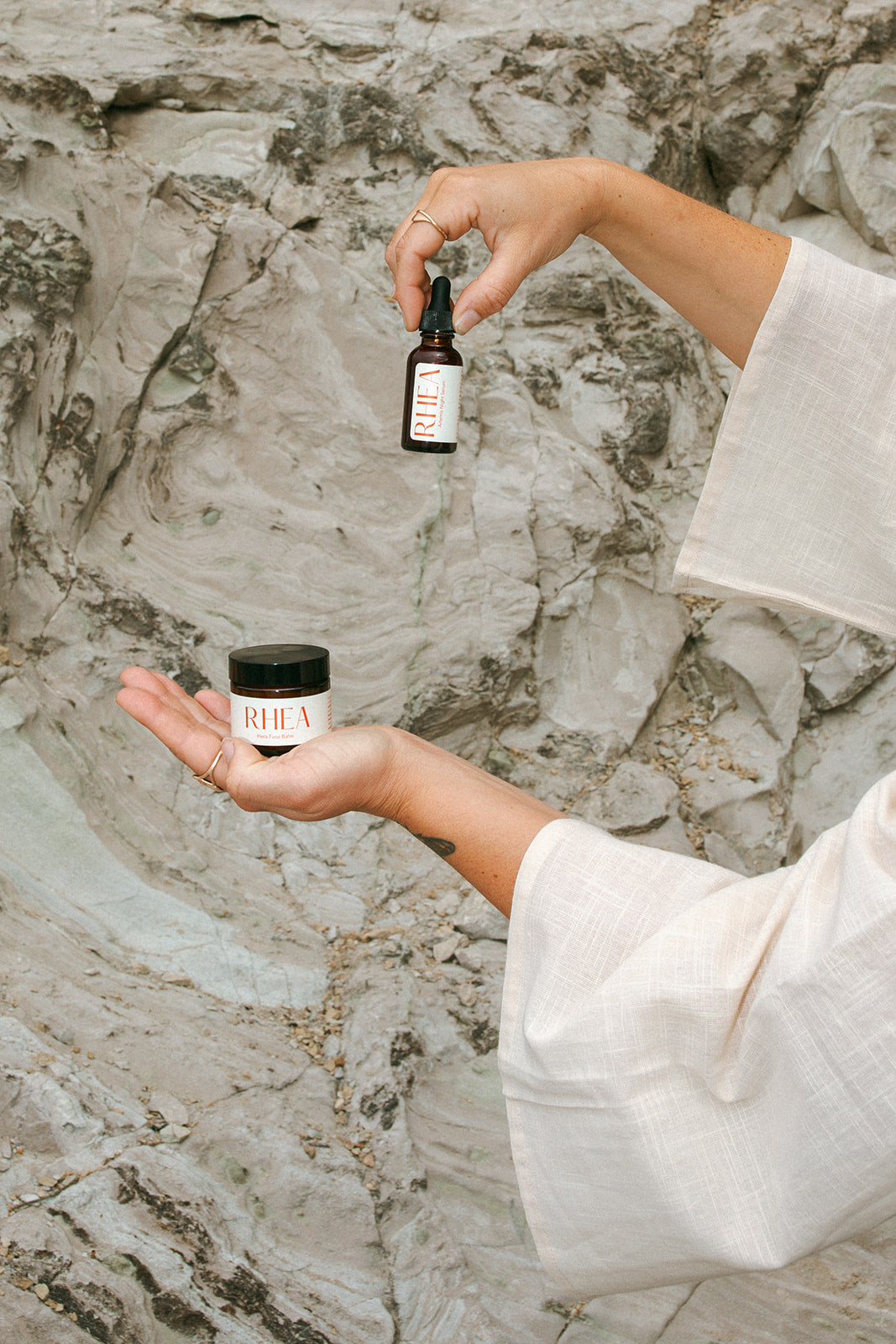 Tallow face balm called HERA and face serum called ARTEMIS from the brand RHEA photographed against a natural stone wall in the ONW 